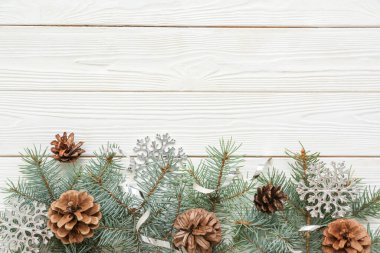 Noel kompozisyonu köknar ağacı dalları, koniler ve beyaz ahşap arka planda kar taneleri. Üst görünüm