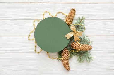 Noel kompozisyonu köknar ağacı dalları, koniler ve beyaz ahşap arka planda yeşil boş kart. Üst görünüm