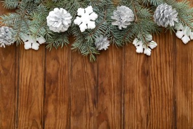 Noel kompozisyonu köknar ağacı dalları, gümüş koniler ve ahşap zemin üzerinde kar taneleri. Üst görünüm