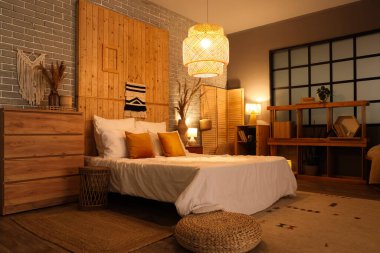 Yatak, çekmece, raf ünitesi ve yatak odasının içinde parlayan lamba.