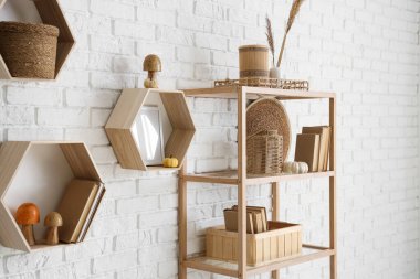 Raflarda kitaplar, mantarlar ve beyaz tuğla duvarın yanında otlar var.