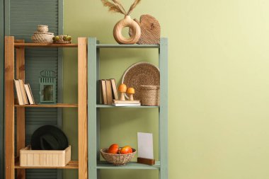 Yeşil duvarın yanında balkabağı, mantar, kitap ve dekor olan raf ünitesi