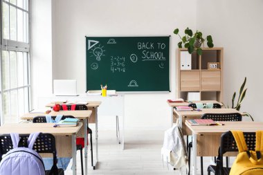 Okul sıraları olan boş sınıfın içi ve karatahtadaki okula geri dönüş metni