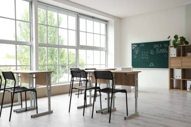 Okul sıraları olan boş sınıfın içi ve karatahtadaki okula geri dönüş metni