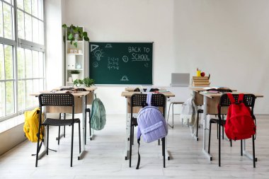 Okul sıraları olan boş sınıfın içi ve karatahtadaki okula geri dönüş metni