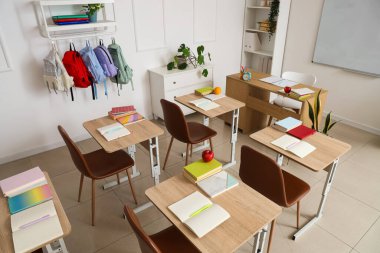 Okul sıralarının ve sırt çantalarının kancalarda asılı olduğu boş sınıfın içi.