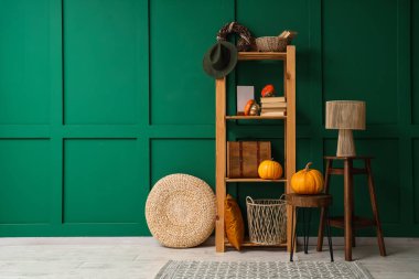 Balkabağı, kitap ve şapkalı ahşap raf ünitesi yeşil duvarın yanında.