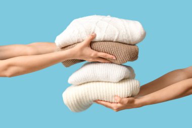 Mavi arka planda sıcak giysi yığını olan kadın elleri