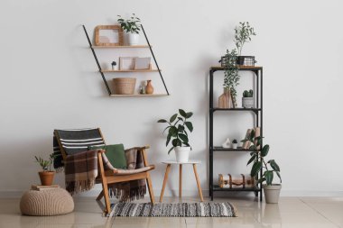 Beyaz duvarın yanında koltuğu, çiçekleri ve raf ünitesi olan modern bir oda.