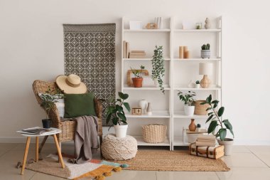 Beyaz duvarın yanında koltuk, ev bitkileri ve raf üniteleri olan modern bir oda.