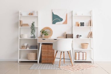 Beyaz duvarın yanında çalışma yeri ve raf üniteleri olan modern bir oda.