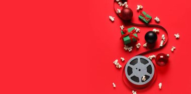 Dağınık patlamış mısır, film makarası, hediye kutuları ve kırmızı arka plandaki süslemeler. Noel filmi konsepti