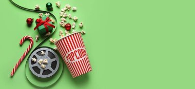 Bir kova patlamış mısır, film makarası, hediye kutusu ve yeşil arka planda mesaj için yeri olan süslemeler. Noel filmi konsepti