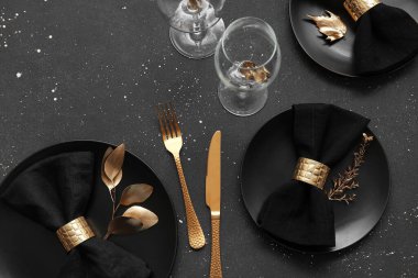 Siyah masa üzerinde altın yapraklar ve çatal bıçak takımı olan zarif bir masa.