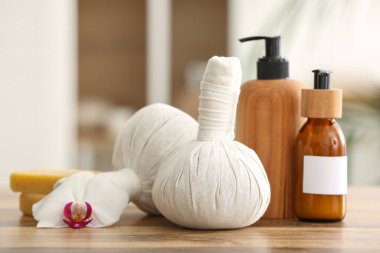 Bitkisel masaj torbaları, kozmetik ürünleri şişeleri ve ahşap masa üzerinde sabun kalıpları.