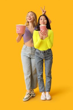 Sarı arka planda patlamış mısır kovaları olan güzel genç kadınlar.