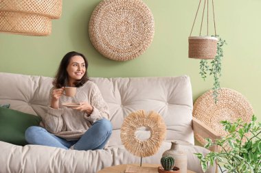 Oturma odasındaki rahat beyaz kanepede dinlenen bir fincan çayla güzel bir genç kadın.