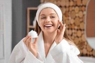 Banyoda duş aldıktan sonra yüz kremi süren genç bir kadın.