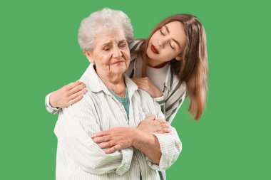 Yeşil arka planda üzgün büyükannesine sarılan genç bir kadın.