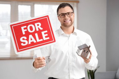 Apartmanında satılık tabelası ve ev modeli olan erkek emlakçı.