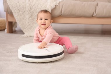 Evdeki halının üzerinde robot süpürgesi olan şirin bir bebek.