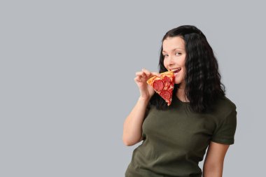 Gri arka planda lezzetli pizzalar yiyen güzel genç bir kadın.