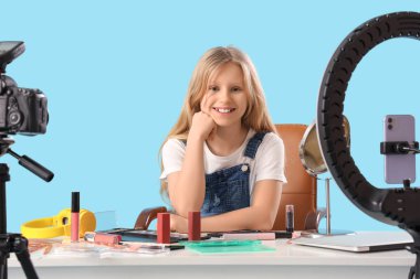 Değişik dekoratif kozmetik kaydına sahip genç güzellik blogcusu mavi arka planda video kaydediyor