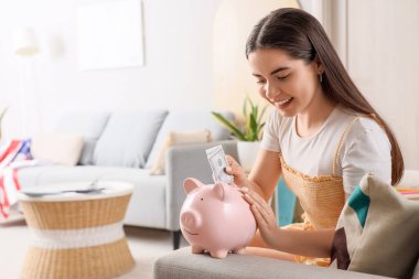 Bayan öğrenci evdeki domuz kumbarasına para yatırıyor.