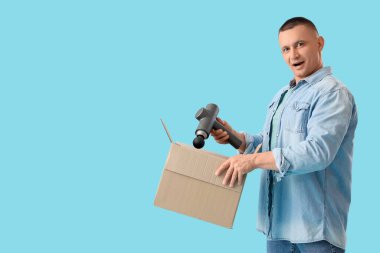 Vurmalı masaj aleti ve mavi arka planda kutusu olan genç bir adam.