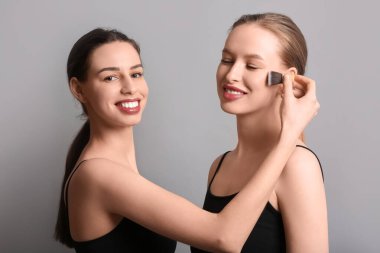 Gri arka planda makyaj yapan kız kardeşler.