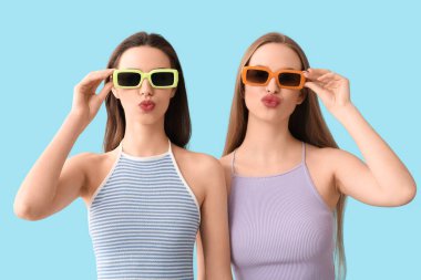 Mavi arka planda güneş gözlüklü güzel kız kardeşler.