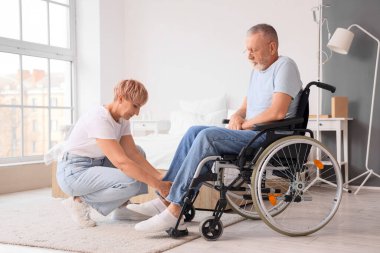 Olgun bir kadın, hasta kocasına tekerlekli sandalyede yardım ediyor.