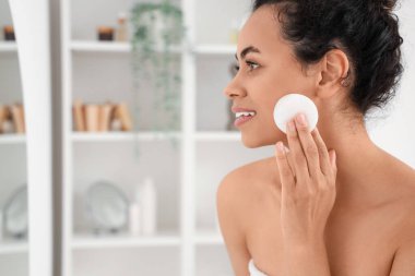 Genç Afro-Amerikalı kadın banyoda pamukla makyaj yapıyor, yakın plan.