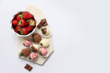 Çikolata kaplı çilek ve gri arka planda bir kase taze çilek.