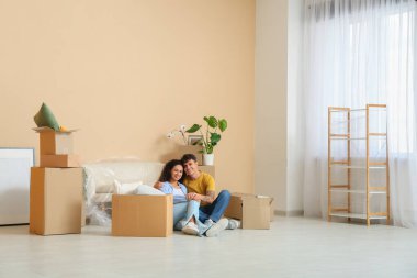 Genç çift karton kutuların yanında oturuyor ve yeni dairelerinde kanepe dolduruyorlar.