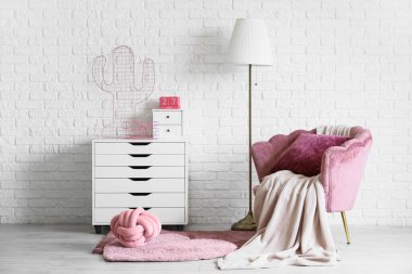 İçinde lamba, pembe koltuk ve çekmeceler olan oturma odası.