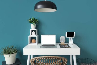 Mavi duvarın yanında dizüstü bilgisayarı, tableti ve bitkisi olan modern bir masa.