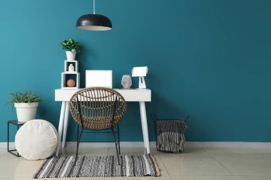 Mavi duvarın yanında dizüstü bilgisayarı, tableti ve bitkisi olan modern bir masa.