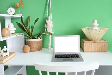 Yeşil duvarın yanında dizüstü bilgisayarı olan modern masa.