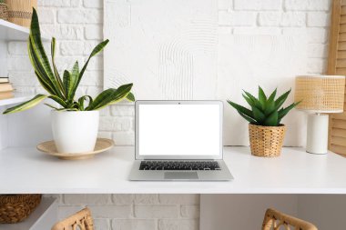 Dizüstü bilgisayarlı şık masa ve beyaz tuğla duvarın yanında bitkiler.