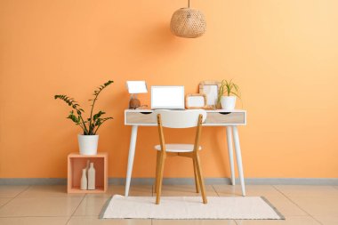 Modern dizüstü bilgisayarı ve turuncu duvarlı tableti olan şık bir masa.