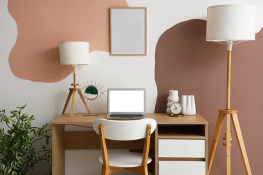 Modern dizüstü bilgisayarı ve beyaz duvarın yanındaki lambası olan şık masa.