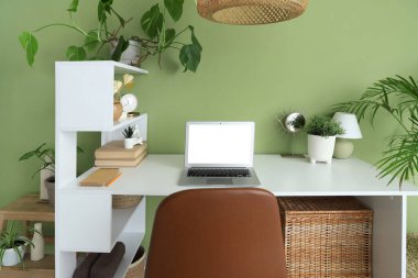 Modern dizüstü bilgisayarlı şık masa ve yeşil duvarın yanındaki ev bitkisi.