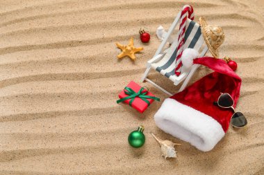 Noel Baba şapkası, oyuncak güverte koltuğu, deniz yıldızı ve kumdaki hediye kutusu. Noel tatili konsepti
