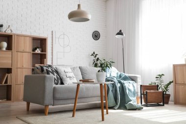 Oturma odasında rahat bir kanepe, sehpa, saksı ve lamba var.