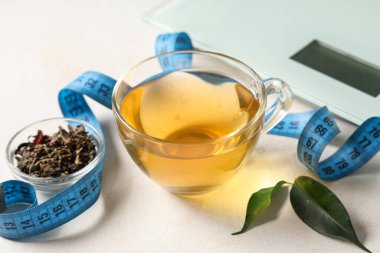Bir fincan diyet çay, kurumuş yapraklar, mezura ve hafif arkaplanda pullar. Kilo verme konsepti