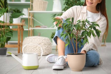 Genç bayan bahçıvan evdeki saksı ve su bidonunun yanında yerde oturuyor.