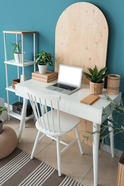 Stylish table with modern laptop and houseplant near blue wall in room