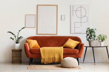 Kahverengi kanepe, ev çiçekleri ve resim çerçeveleri oturma odasındaki beyaz duvarda.