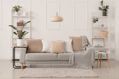 Gri kanepe, ev çiçekleri ve raflar oturma odasındaki beyaz duvarın yanında.